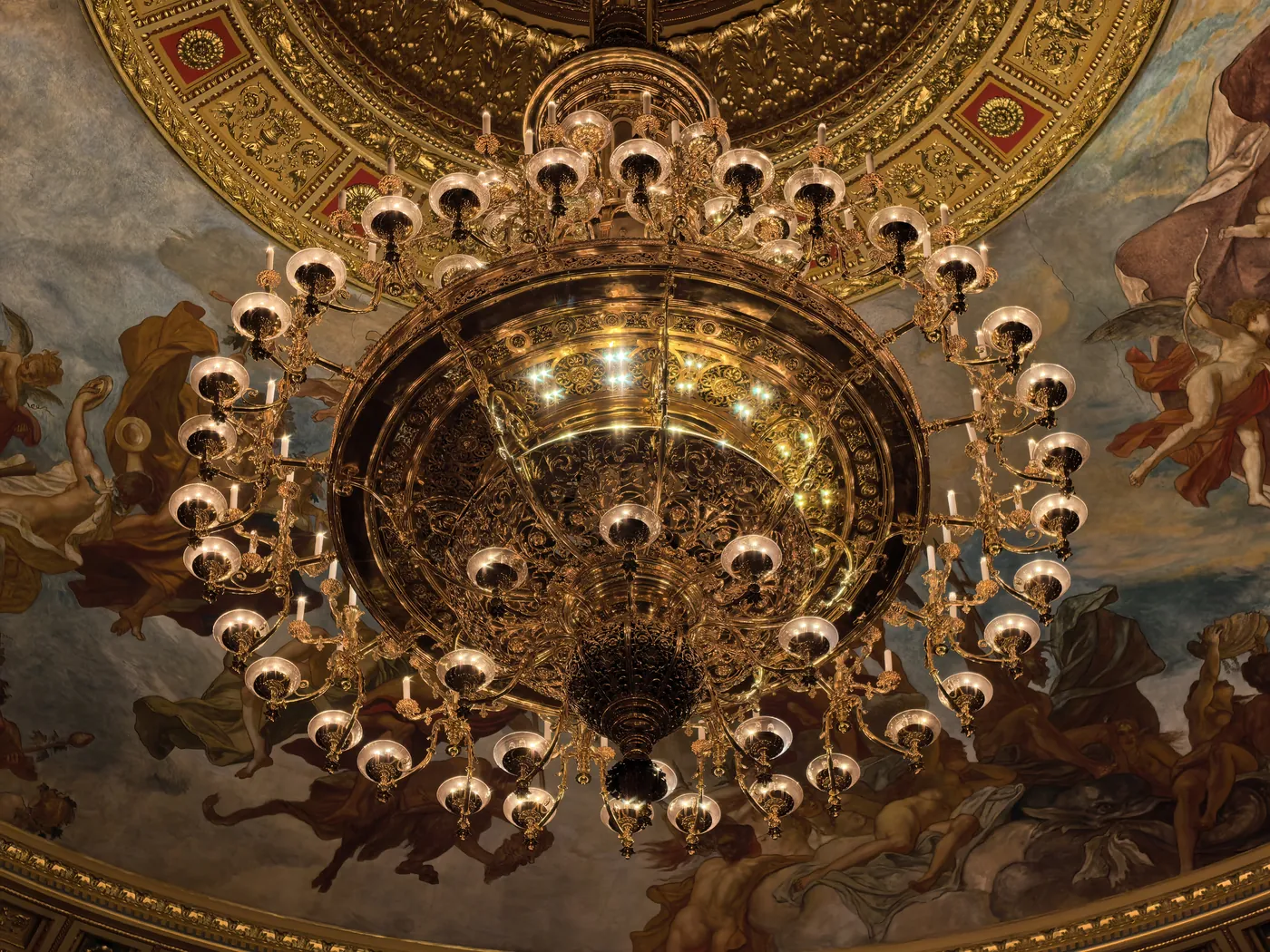 A gilded chandelier seen from below against the painted ceiling of the auditorium
